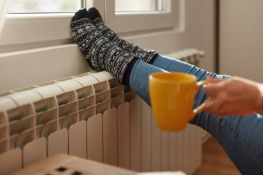 Soğuk bir kış gününde ayakları ısıtan kadın, enerji ve gaz krizi, soğuk oda, ısıtma sorunları.