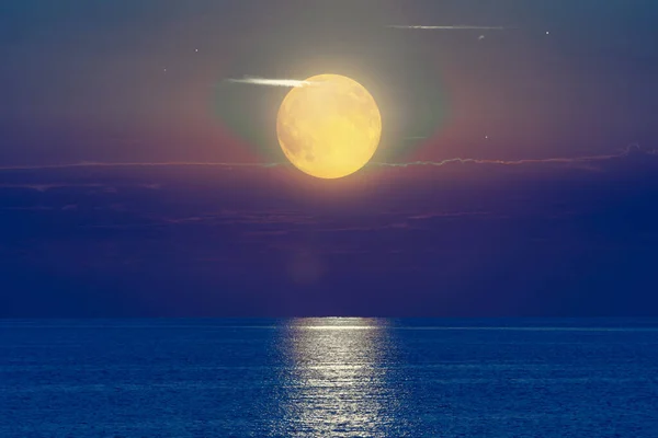 Moon with starry skies above ocean horizon.