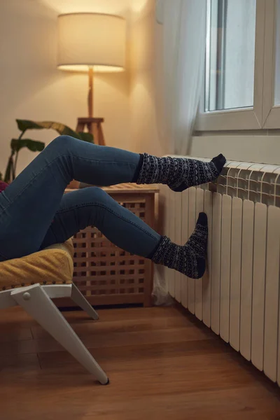 Woman heating feet on a chilly winter day, energy and gas crisis, cold room, heating problems.