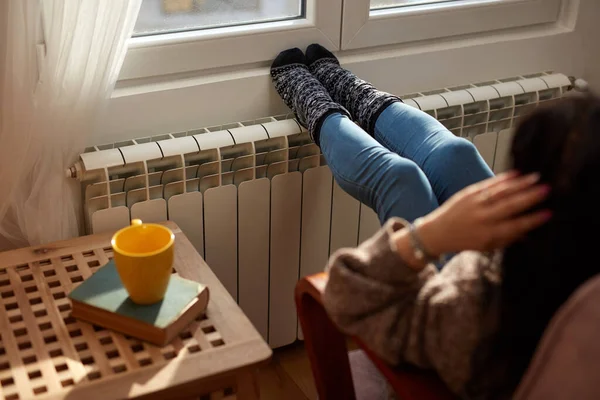 Woman heating feet on a chilly winter day, energy and gas crisis, cold room, heating problems.