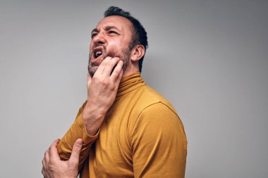 Diş ağrısı çeken yetişkin bir adam acı dolu bir yüz ifadesi takınıyor..
