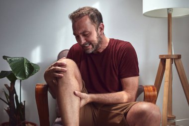 Diz ağrısı, çıkık, uyuşukluk, kramp ve evdeki diğer eklem sorunları olan yetişkin bir adam..