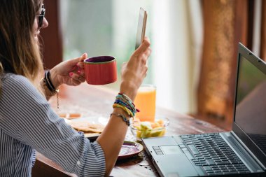 Akıllı telefon ve dizüstü bilgisayar kullanan genç bir kadın, ev konseptiyle çalışıyor..