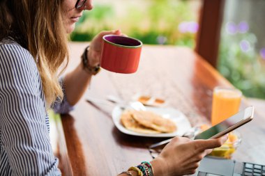 Akıllı telefon ve dizüstü bilgisayar kullanan genç bir kadın, ev konseptiyle çalışıyor..