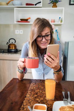 Modern bir evde akıllı telefon kullanan genç bir kadın..