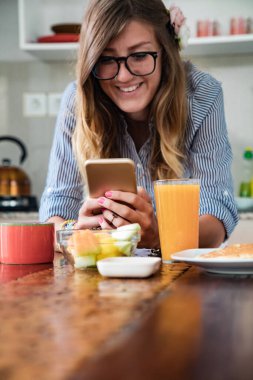 Modern bir evde akıllı telefon kullanan genç bir kadın..