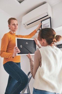 Anne ve kızı merdivene resim ve fotoğrafları asıyorlar evdeki rafa ve duvara..