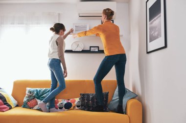 Anne ve kızı kanepede duruyor, resimlerini ve fotoğraflarını evdeki raflara asıyorlar..