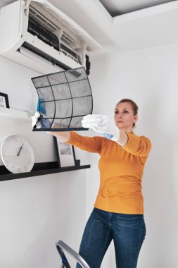Kadın evdeki havalandırma filtrelerini temizliyor..