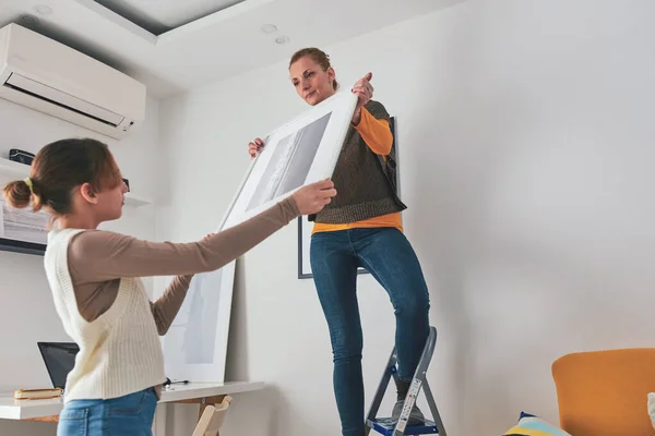 stock image Mother and daughter hanging pictures and photos at home.