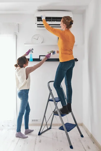 Mother and daughter cleaning aircon filters indoor unit at home.