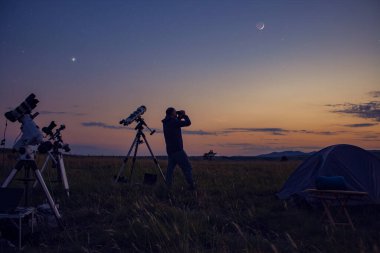 Astronomik teleskoplu bir adam Samanyolu yıldızlarının altında gece gökyüzünü gözlemliyor..
