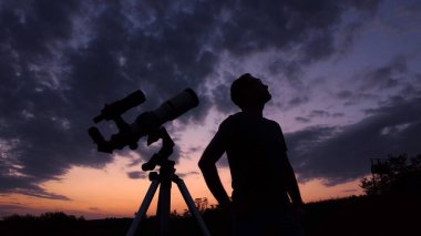 Astronomik teleskoplu bir adam Samanyolu yıldızlarının altında gece gökyüzünü gözlemliyor..