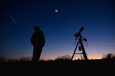 Silhouette of a man, telescope and countryside under evening skies. clipart
