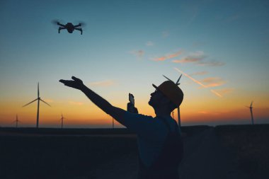 Bir yel değirmeni çiftliği parkında teftiş için İHA kullanan mühendis..