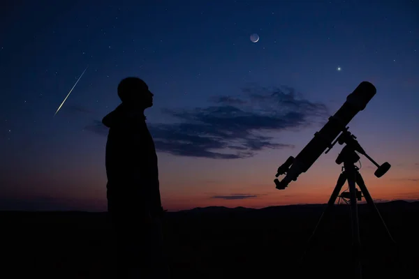 Man with astronomical telescope observing night sky, under the Mlky way stars.