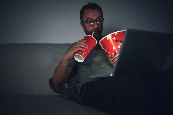 Adult man watching movies at home, eating popcorn and drinking juice.