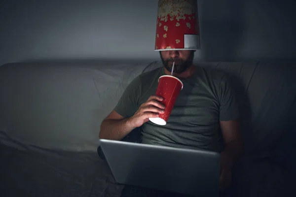 Adult man watching movies at home, eating popcorn and drinking juice.