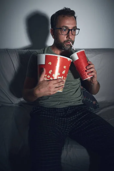 Adult man watching movies at home, eating popcorn and drinking juice.