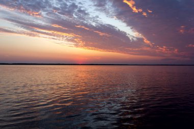 Volga Nehri 'nde şafak vakti, güneş ufuktan yükselir ve güzel bir şekilde bulutları kırmızı ışıkla aydınlatır, suda güneşli bir yol.