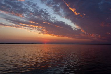 Volga Nehri 'nde şafak vakti, güneş ufuktan yükselir ve güzel bir şekilde bulutları kırmızı ışıkla aydınlatır, suda güneşli bir yol.