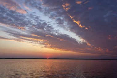 Volga Nehri 'nde şafak vakti, güneş ufuktan yükselir ve güzel bir şekilde bulutları kırmızı ışıkla aydınlatır, suda güneşli bir yol.