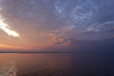 Volga Nehri 'nde şafak vakti, güneş ufuktan yükselir ve güzel bir şekilde bulutları kırmızı ışıkla aydınlatır, suda güneşli bir yol.