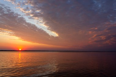 Volga Nehri 'nde şafak vakti, güneş ufuktan yükselir ve güzel bir şekilde bulutları kırmızı ışıkla aydınlatır, suda güneşli bir yol.