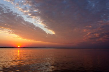 Volga Nehri 'nde şafak vakti, güneş ufuktan yükselir ve güzel bir şekilde bulutları kırmızı ışıkla aydınlatır, suda güneşli bir yol.