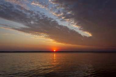 Volga Nehri 'nde şafak vakti, güneş ufuktan yükselir ve güzel bir şekilde bulutları kırmızı ışıkla aydınlatır, suda güneşli bir yol.