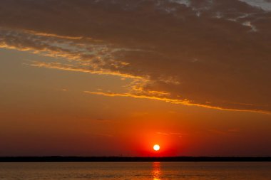 Volga Nehri 'nde şafak vakti, güneş ufuktan yükselir ve güzel bir şekilde bulutları kırmızı ışıkla aydınlatır, suda güneşli bir yol.