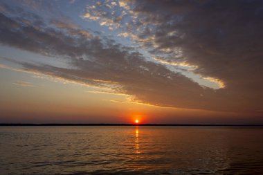 Volga Nehri 'nde şafak vakti, güneş ufuktan yükselir ve güzel bir şekilde bulutları kırmızı ışıkla aydınlatır, suda güneşli bir yol.
