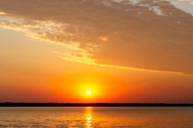 Volga Nehri 'nde şafak vakti, güneş ufuktan yükselir ve güzel bir şekilde bulutları kırmızı ışıkla aydınlatır, suda güneşli bir yol.