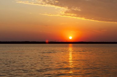 Volga Nehri 'nde şafak vakti, güneş ufuktan yükselir ve güzel bir şekilde bulutları kırmızı ışıkla aydınlatır, suda güneşli bir yol.