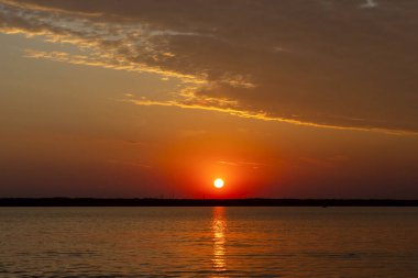 Volga Nehri 'nde şafak vakti, güneş ufuktan yükselir ve güzel bir şekilde bulutları kırmızı ışıkla aydınlatır, suda güneşli bir yol.