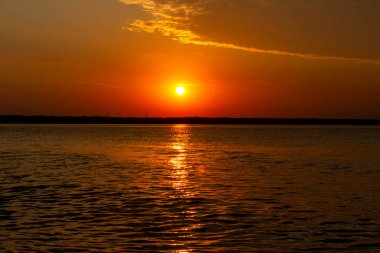 Volga Nehri 'nde şafak vakti, güneş ufuktan yükselir ve güzel bir şekilde bulutları kırmızı ışıkla aydınlatır, suda güneşli bir yol.