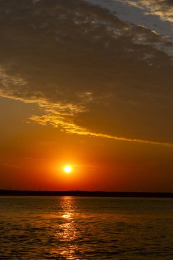 Volga Nehri 'nde şafak vakti, güneş ufuktan yükselir ve güzel bir şekilde bulutları kırmızı ışıkla aydınlatır, suda güneşli bir yol.