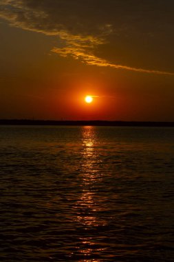 Volga Nehri 'nde şafak vakti, güneş ufuktan yükselir ve güzel bir şekilde bulutları kırmızı ışıkla aydınlatır, suda güneşli bir yol.
