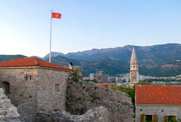 Montenegro - Budva: 8 de septiembre de 2021: Bandera de Montenegro sobre el fondo de la ciudad de Budva y las montañas. Bandera de Montenegro ondea sobre el casco antiguo — Foto de Stock