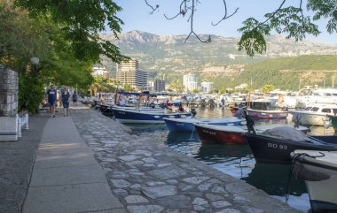 Karadağ - Budva: 9 Eylül 2021: Pek çok yelkenli yat, tekne ve dağ manzaralı yürüyen insanlarla dolu bir liman. Limanı ve turistleriyle Budva turistik kenti manzarası