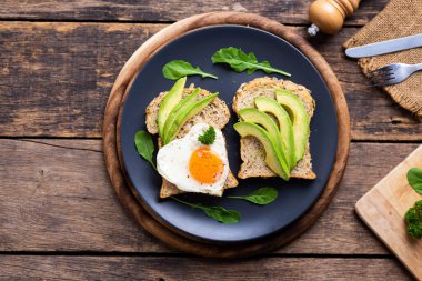 Buğday ekmeğinde dilimlenmiş Avokado, ahşap masada kızarmış yumurtalı Avokado Sandviçi.