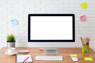 Boş beyaz ekranlı bilgisayar ve ahşap bir masada ofis malzemeleri olan çalışma alanı.