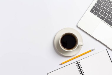 Not defteri, dizüstü bilgisayarı ve kahve fincanı olan beyaz ofis masası, beyaz arka planda ofis malzemeleri.