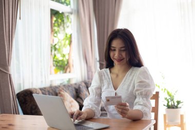 İnternetten alışveriş yapmak. Genç bir kadın elinde dizüstü bilgisayar kullanarak kredi kartı tutuyor. İş kadını evden çalışıyor.
