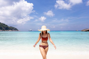 Hasır şapkalı ve turuncu bikinili bir kadın güzel mavi gökyüzü olan sahilde dinleniyor. Similan Adası Phuket Tayland 'da, yaz tatili konsepti.