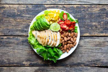 Sağlıklı yemek, sebze salatası, tavuk ve badem, ahşap bir masada beyaz bir tabakta. Üst görünüm