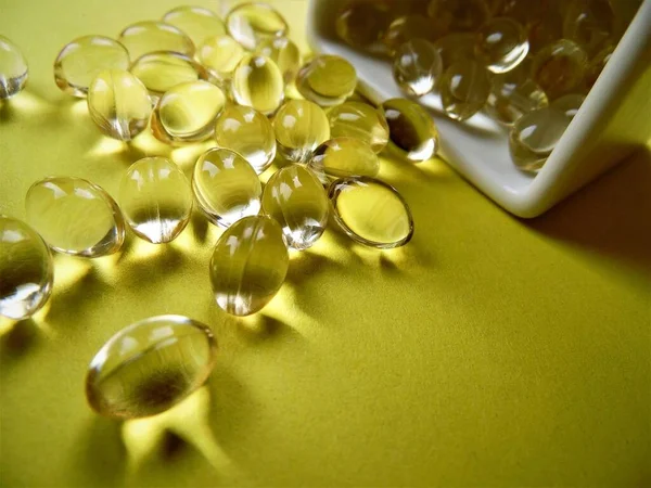 transparent capsules with vitamins on a yellow background close-up