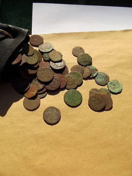 antique copper coins of the 17th century, scattered from a leather wallet on a light background, close-up, a quarter of a penny