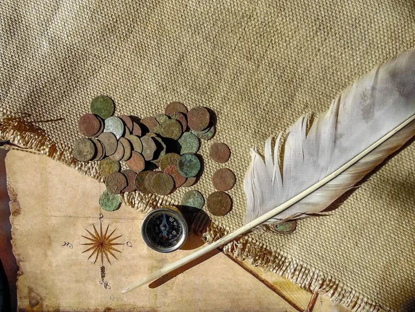 antique copper coins and an eagle feather against the background of an old map and burlap, installation for a treasure hunter