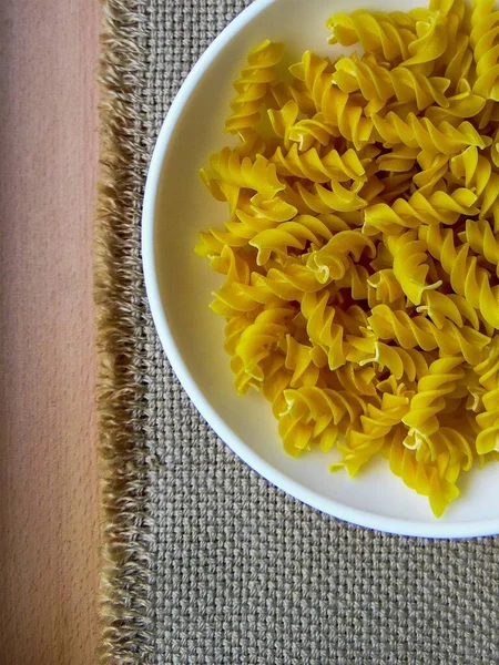 twisted pasta on a light dish against the background of coarse cloth